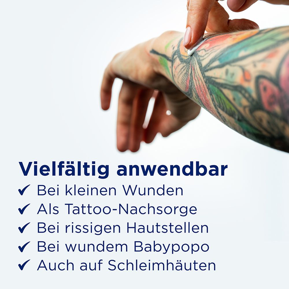 Hand mit Tattoo, Salbe wird aufgetragen. Text: Vielfältig anwendbar: kleine Wunden, Tattoo-Nachsorge, rissige Hautstellen, wunde Babypopo, Schleimhäute.