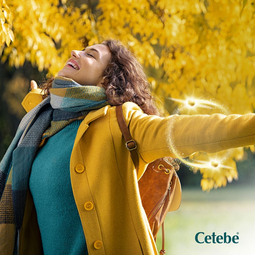 Frau im Herbstlaub. Trägt gelbe Jacke und Schal. Cetebe Logo unten rechts.