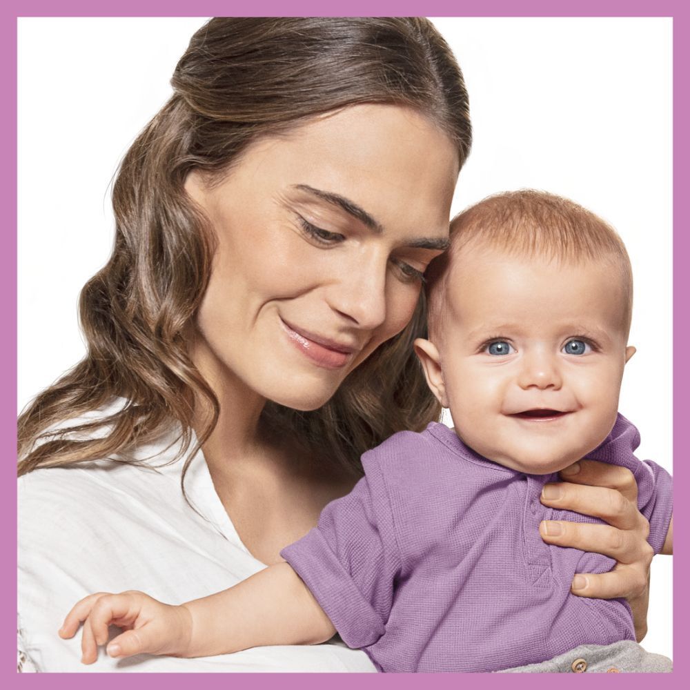 Frau hält Baby. Baby trägt lila Kleidung. Beide lächeln. Hintergrund weiß.