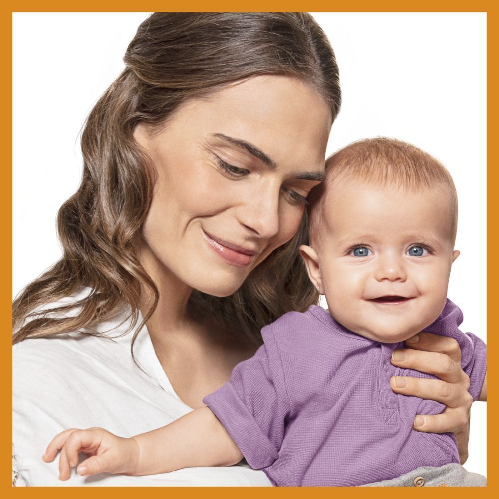Frau hält Baby. Baby lächelt. Baby trägt lila Shirt.