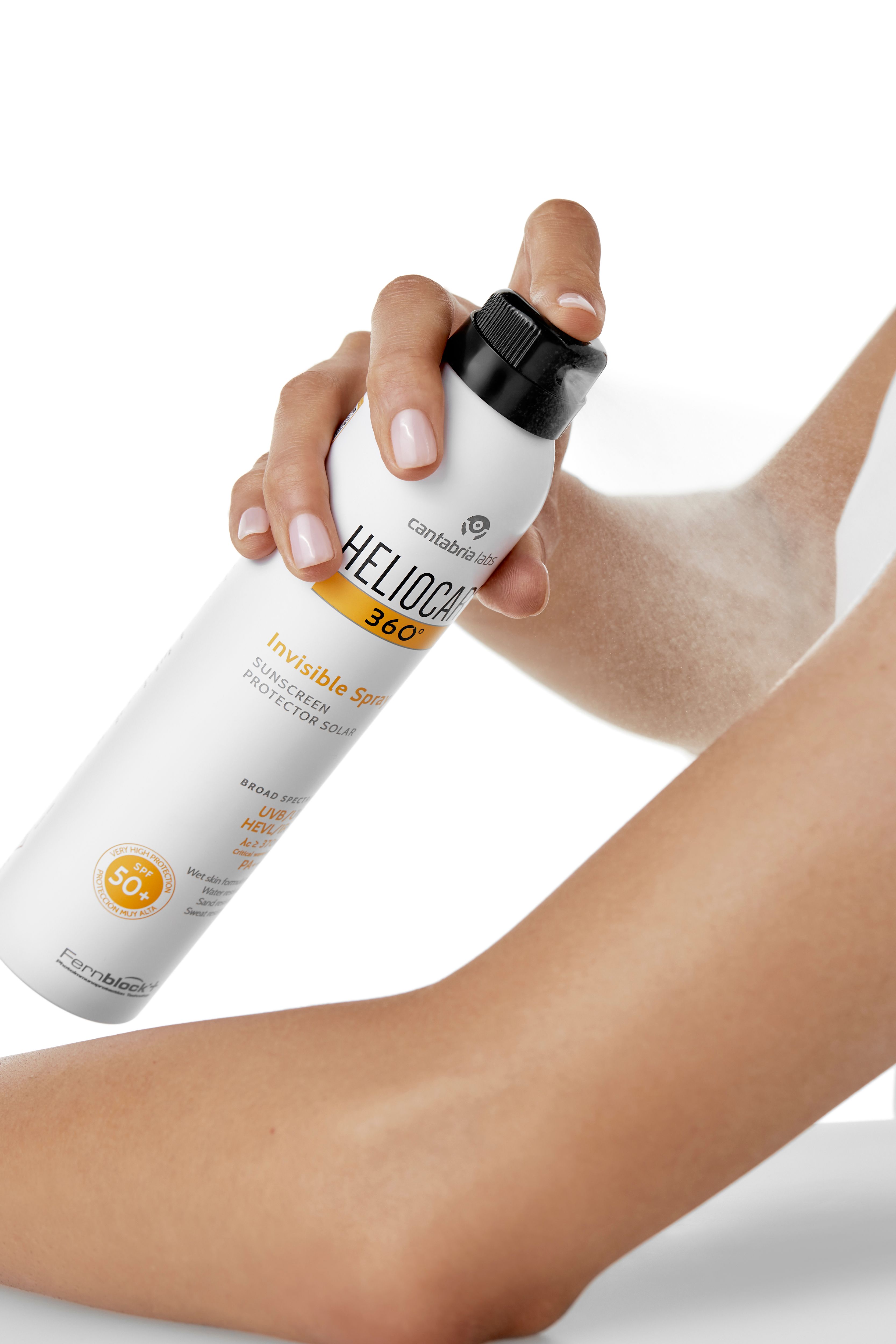Person sprüht Spray auf Arm. Spraydose: HELIOCARE 360° Invisible Spray, LSF 50+. Weiß, schwarzer Deckel.