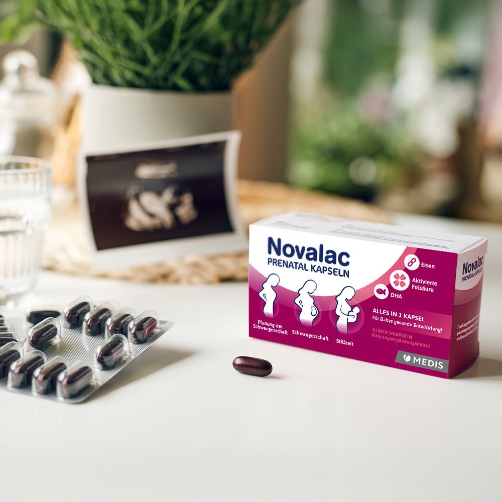 Novalac PRENATAL KAPSELN Packung und Kapseln auf Tisch. Im Hintergrund: Ultraschallbild, Glas Wasser. 10 Weichkapseln.