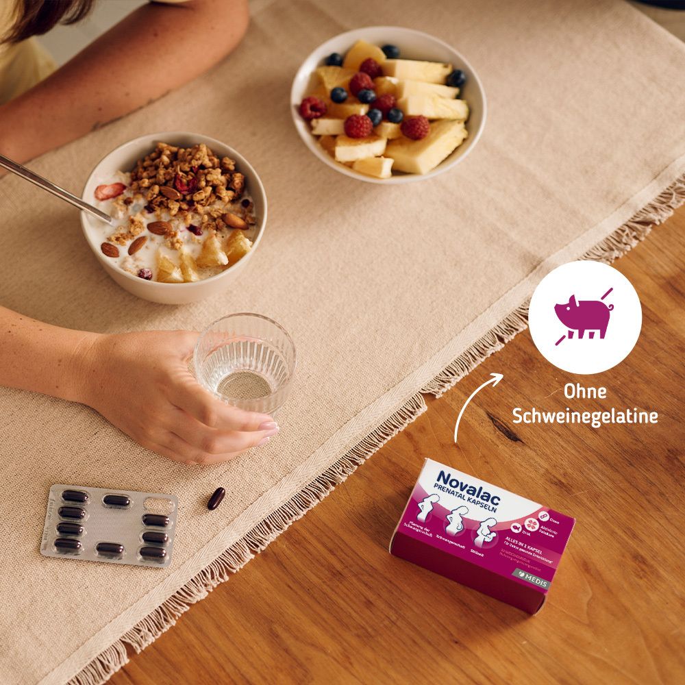 Tisch mit Obst, Wasser, Kapseln und Novalac PRENATAL KAPSELN Packung. Symbol: Ohne Schweinegelatine. Hand mit Löffel.