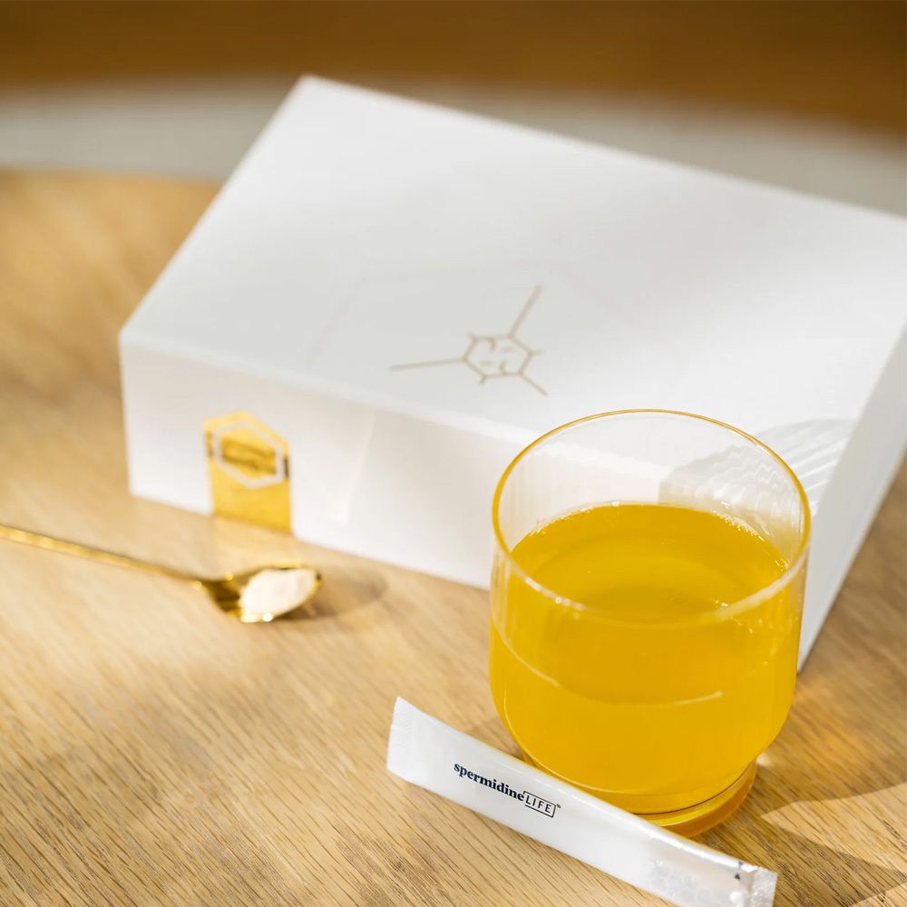 Glas mit gelbem Getränk, Löffel mit Substanz, Beutel mit Schriftzug spermidineLIFE.