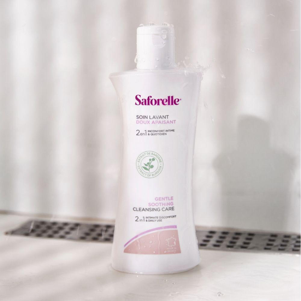 Witte Saforelle fles onder water. Tekst Soin Lavant Doux Apaisant. Achtergrond: doucheruimte.