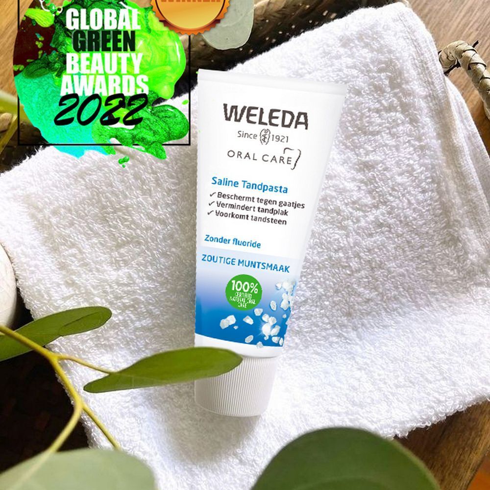 Tube de dentifrice Weleda Saline sur serviette blanche. Avec logo Global Green Beauty Awards 2022. Fond : bois et feuilles.