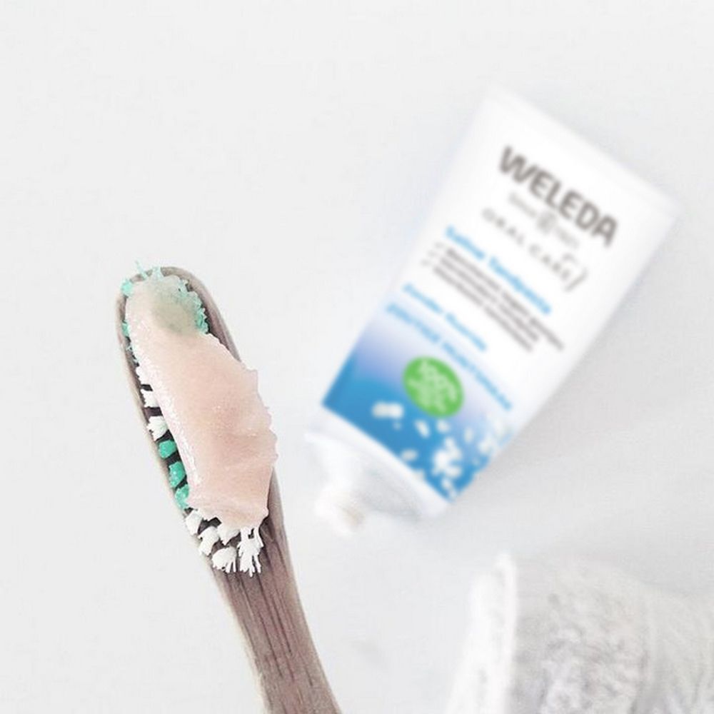 Brosse à dents avec dentifrice et tube de dentifrice Weleda Saline. Dentifrice rose. Tube avec texte bleu et vert.