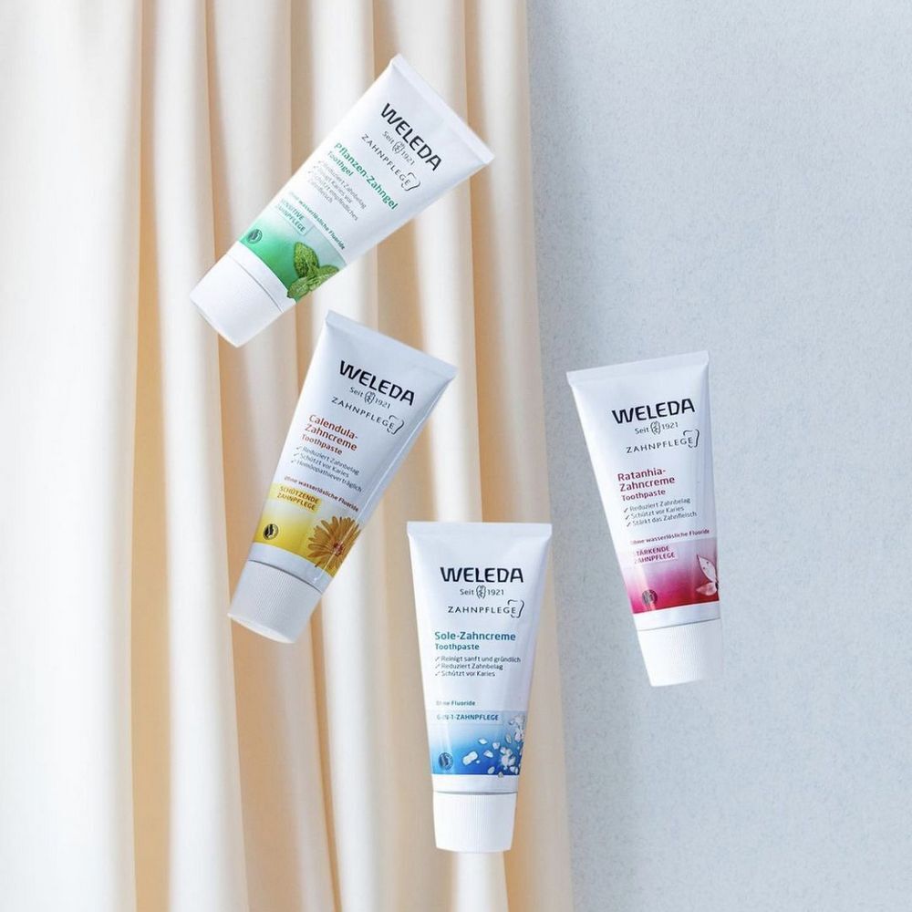 Quatre tubes de dentifrice Weleda. Différentes variétés, avec différentes couleurs et inscriptions. Flottant sur fond clair.