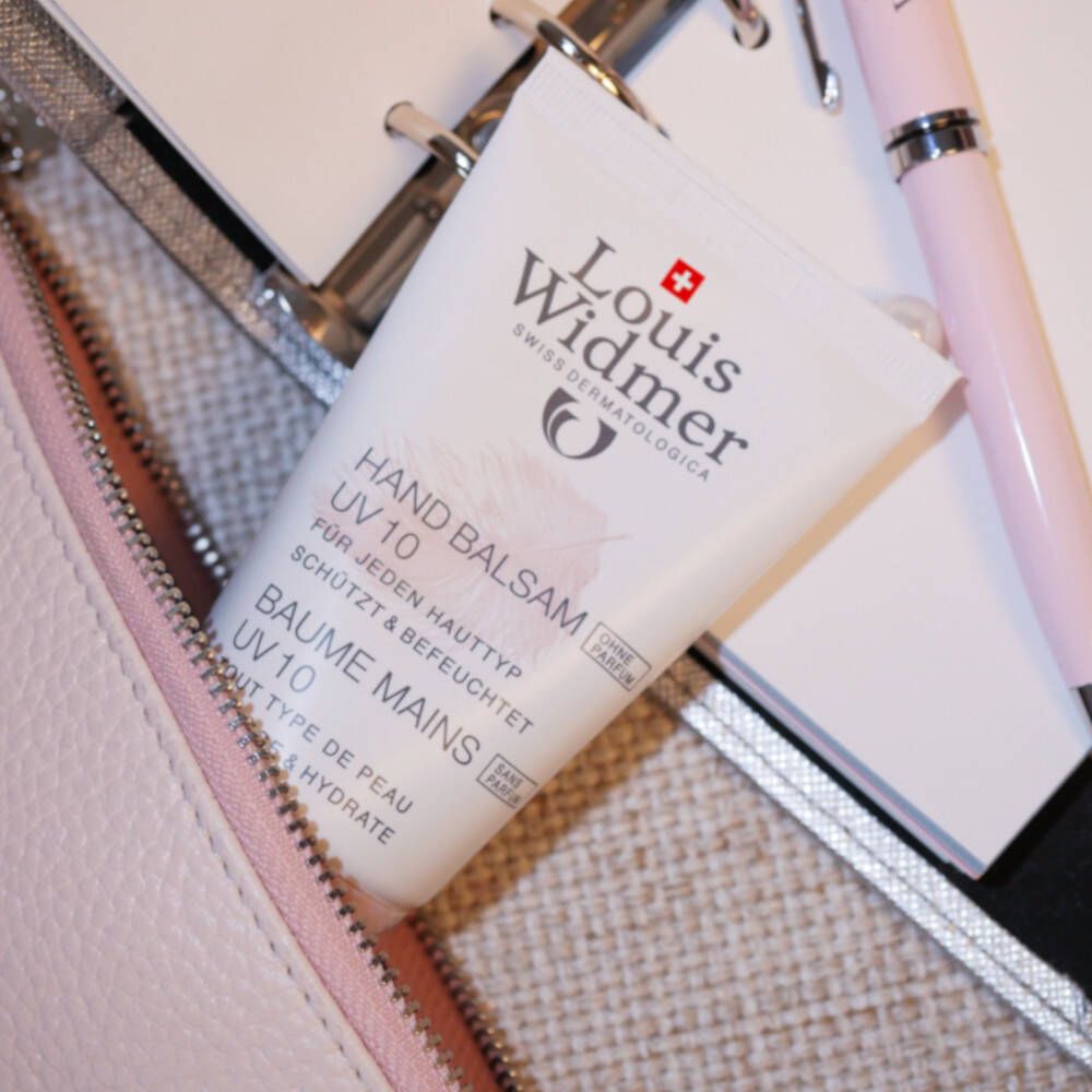 Tube de baume pour les mains blanc avec bouchon rose, dans un sac rose. Inscription: Louis Widmer, Hand Balsam UV 10.