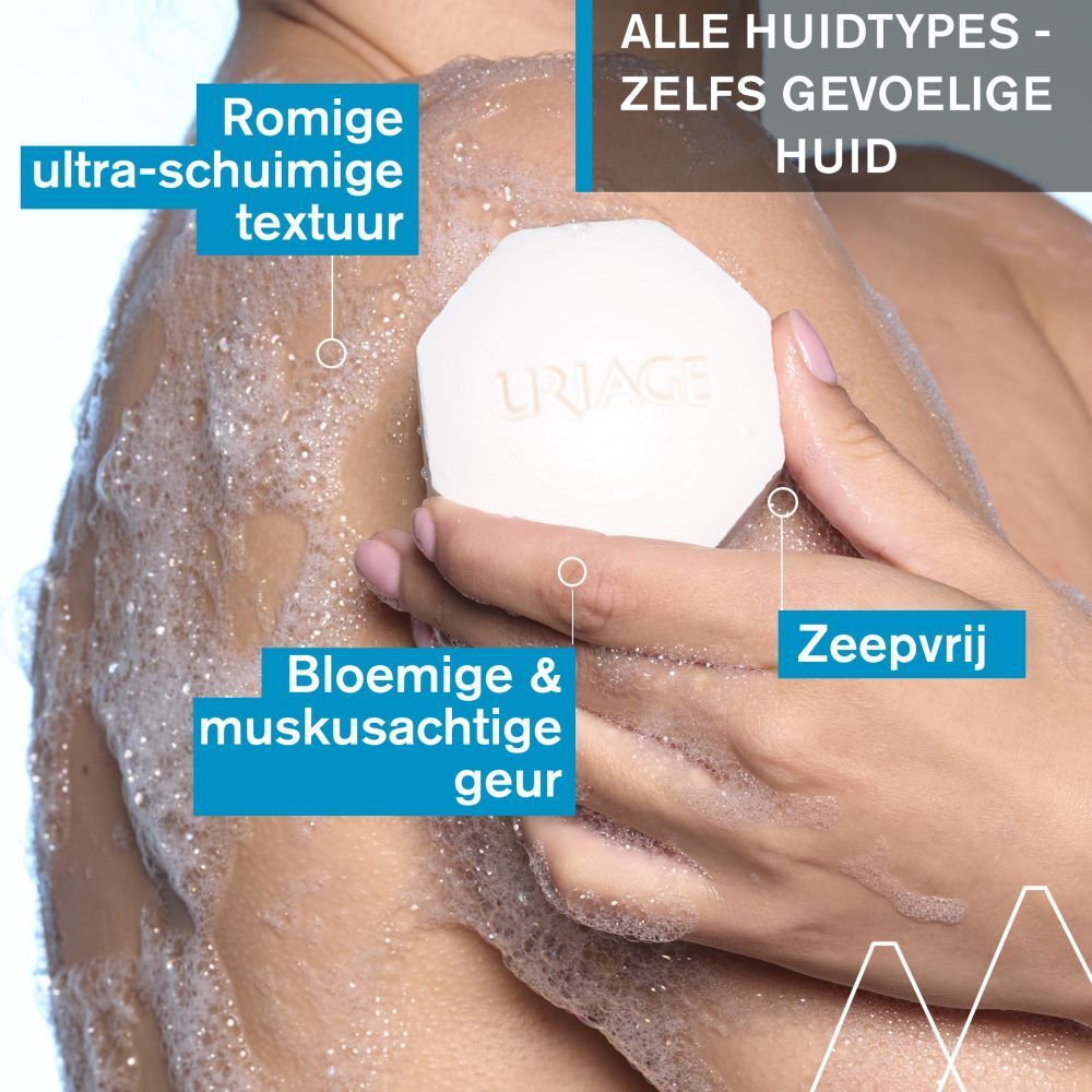 Persoon die zeep gebruikt. Achthoekige zeep met Uriage-logo. Tekst: ultra-schuimige textuur, bloemige geur, zonder zeep.