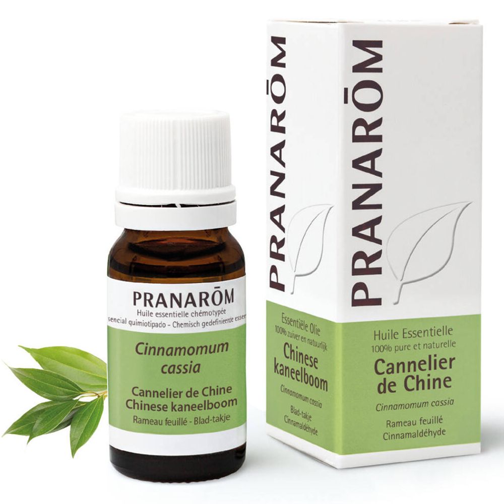 Flacon en verre brun avec bouchon blanc et étiquette. Boîte et feuilles à côté. Inscription : Pranarôm, Cannelle de Chine.