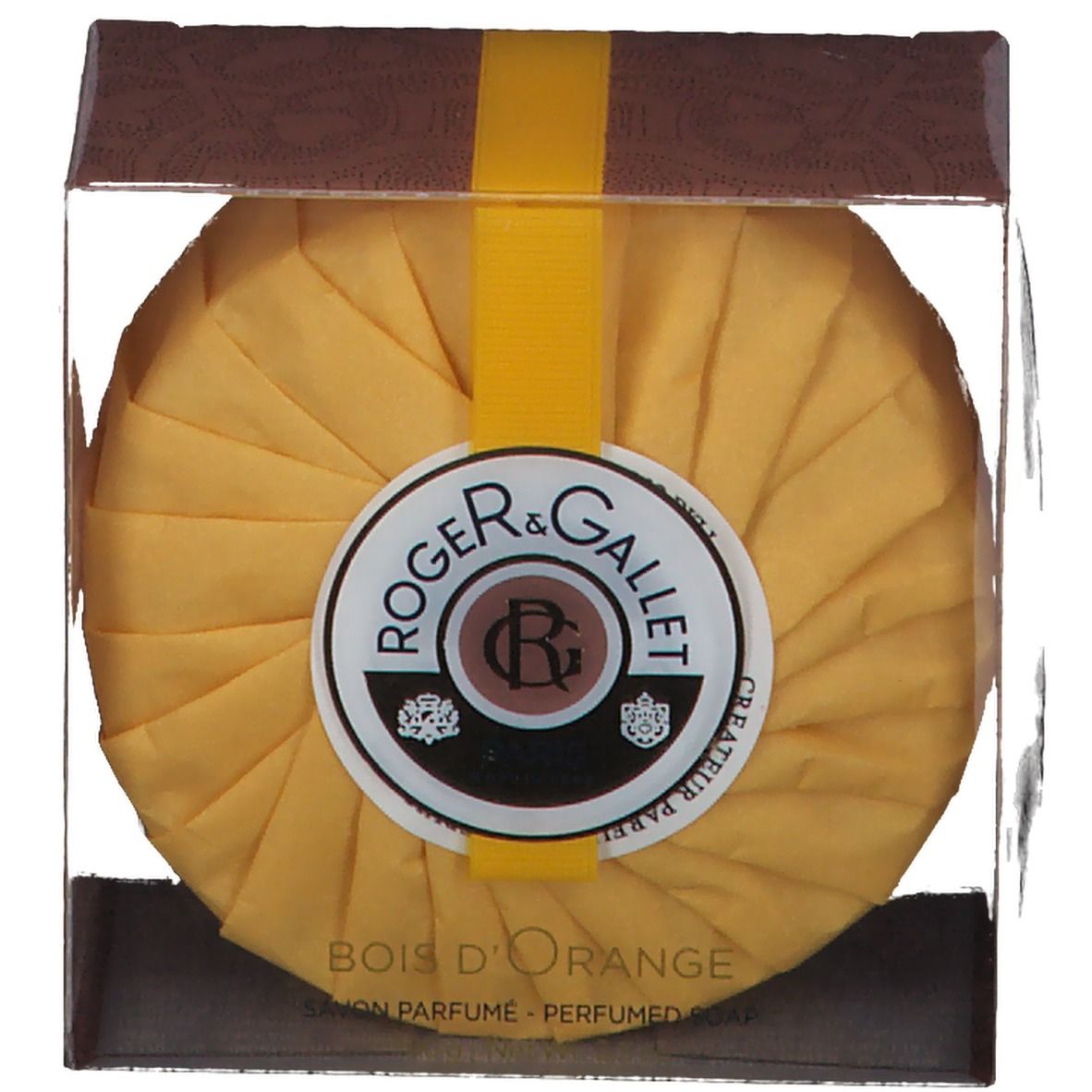Ronde gele zeep in transparante doos. Geel lint. Etiket: ROGER & GALLET, Bois d'Orange. Tekst.