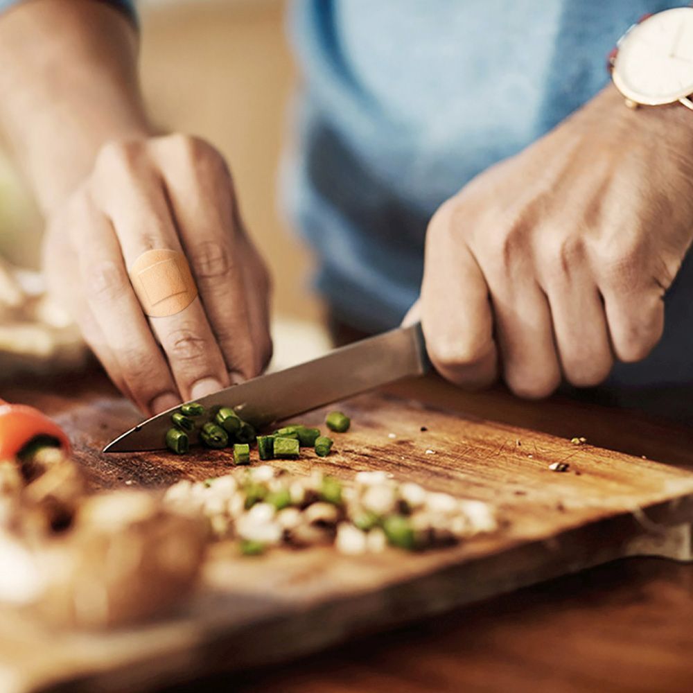 Man snijdt groenten met pleister op vinger. Pleister beige, rechthoekig.