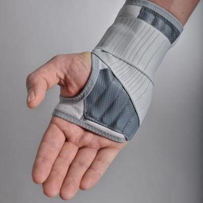 Attelle de poignet grise et blanche sur le poignet. Maille, ouverture pour le pouce. Fermetures velcro. Vue de dessus.