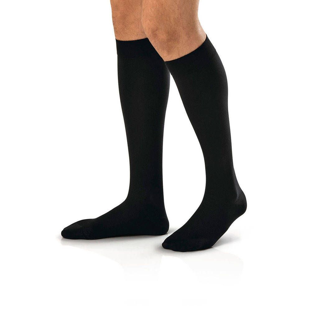 Bas de compression noirs sur les jambes d'une personne. Les bas montent jusqu'aux genoux.
