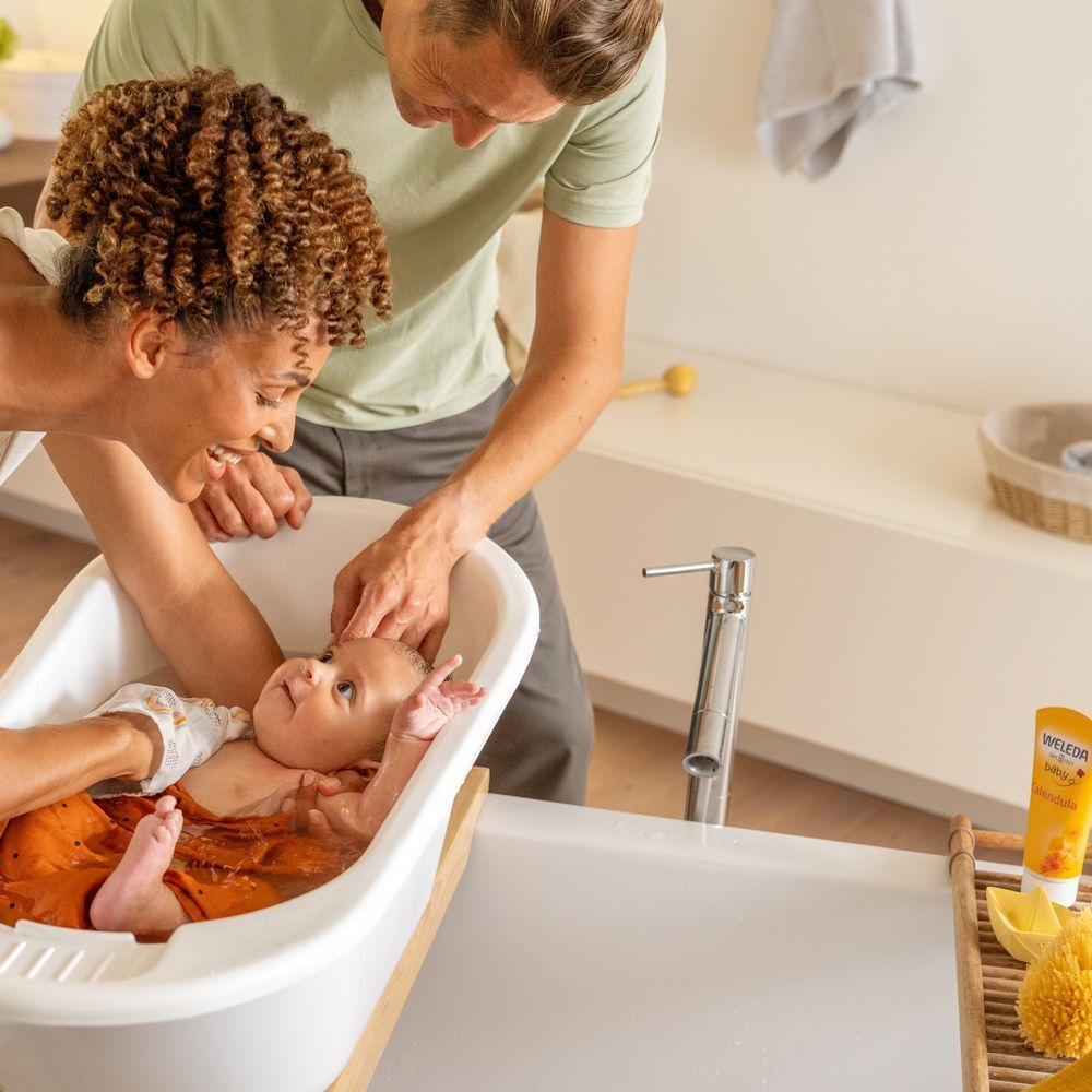 Un bébé est baigné par ses parents dans une baignoire pour bébé. Le bébé est dans l'eau. Une personne tient le bébé.
