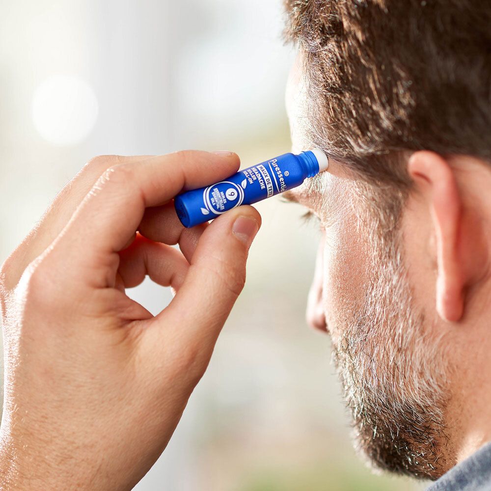 Blaue Roll-on-Flasche mit Applikator in der Hand eines Mannes, der sie auf die Schläfe aufträgt.
