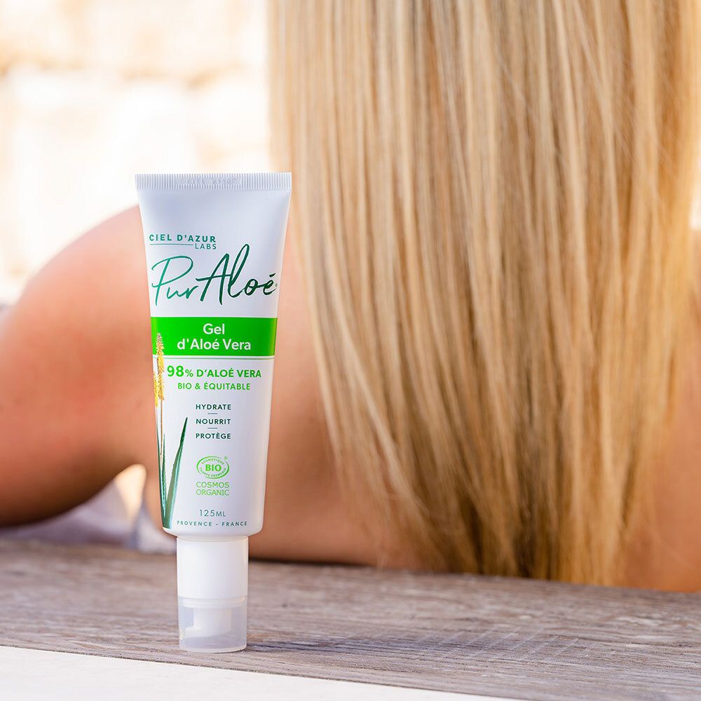 Tube blanc avec impression verte, à côté d'une personne. Texte : PurAloé Vera Gel d'Aloé Vera. Certification bio.