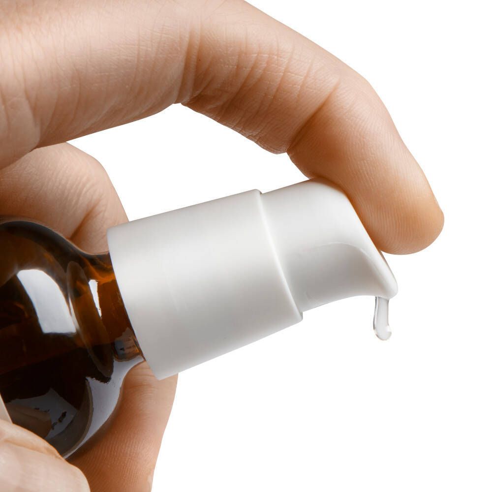 Gros plan d'une main appuyant sur une pompe blanche. Du liquide coule du distributeur.