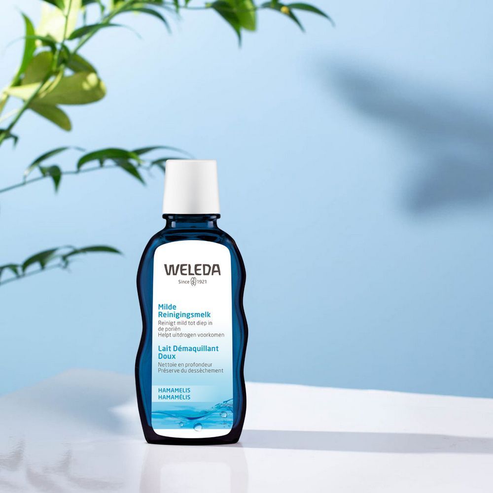 Blaue Weleda-Flasche mit weißem Deckel. Produktinformationen auf der Flasche. Hintergrund mit Wasser und Blättern.