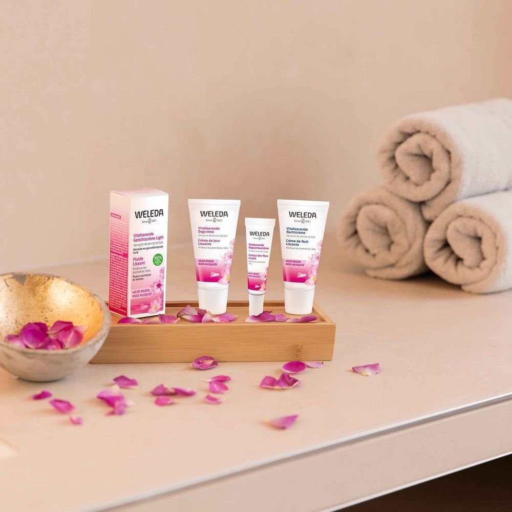 Weleda Crème de Jour Lissante Produkte auf Tablett. Produkte, Verpackung, Blütenblätter und Handtücher. Logo Weleda.