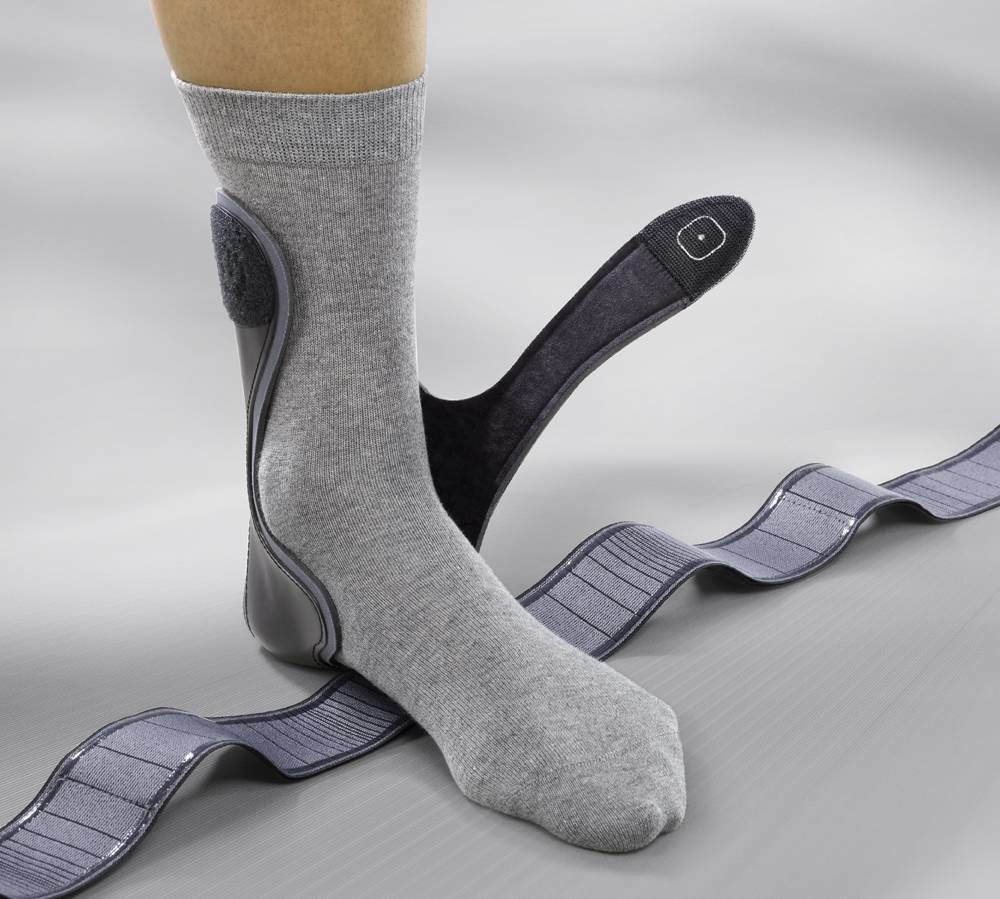 Orthèse de cheville avec bande, portée sur une jambe. Chaussette grise. Éléments noirs. Bande à rayures grises.