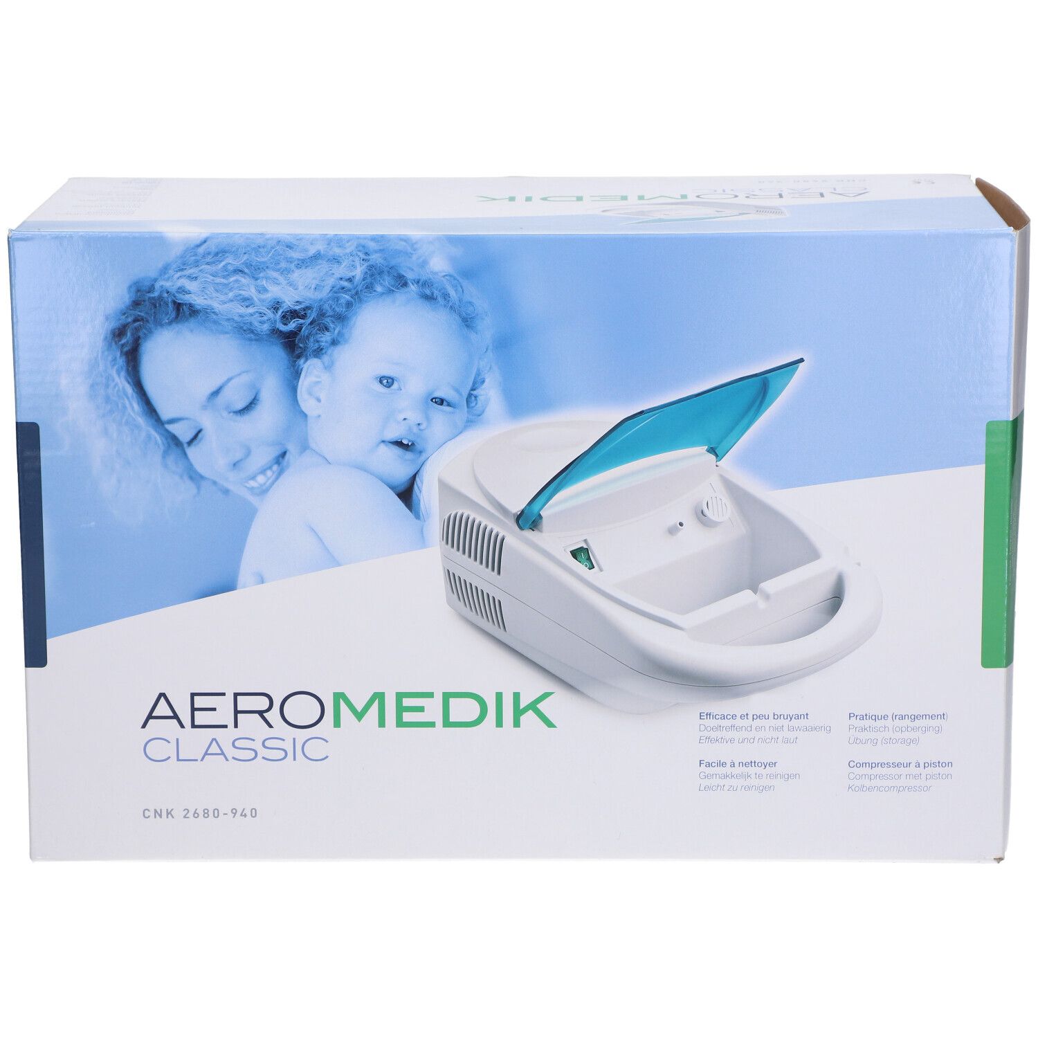 Aérosol Medik Classic dans son emballage. Appareil blanc avec couvercle bleu. Inscription: AERO MEDIK CLASSIC. Textes multilingues.