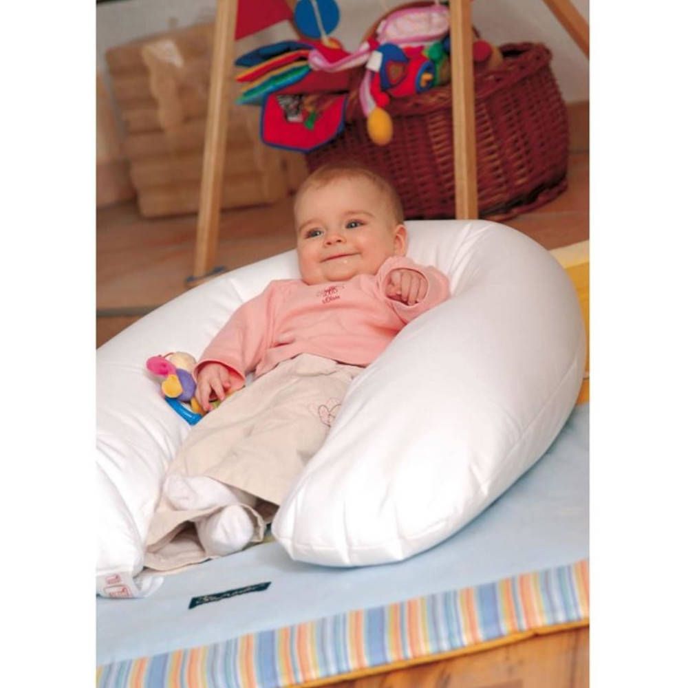 Bébé assis dans un coussin blanc en forme de U. Sur fond bleu. L'enfant regarde la caméra.