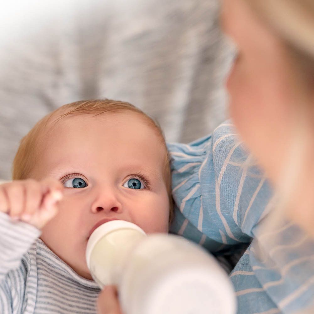 Bébé buvant au biberon. Personne tenant le biberon. Vue rapprochée.