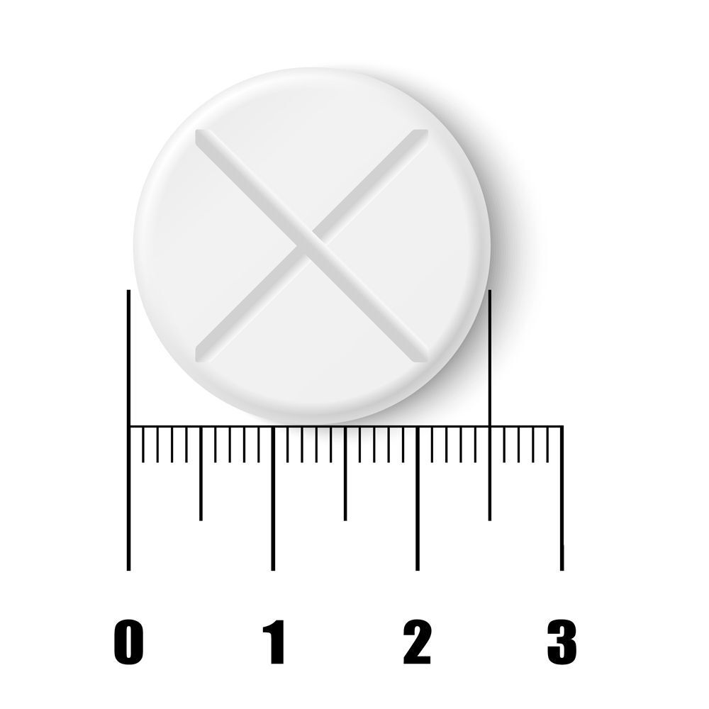 Comprimé rond blanc avec une entaille en croix. Règle pour la taille.