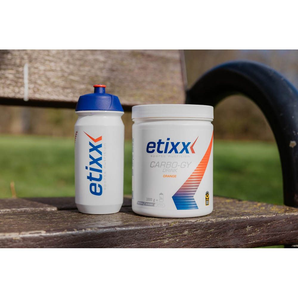 Etixx drinkfles en pot Carbo-Gy Orange op een houten bank. Beide wit met blauwe en rode accenten.