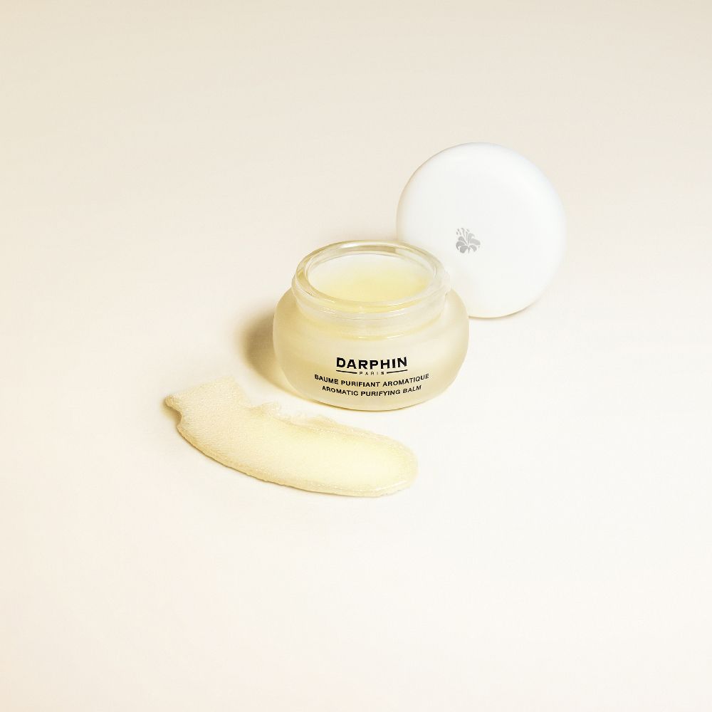 Pot ouvert avec baume jaune, à côté une noisette. Couvercle à côté. Inscription : Darphin, Baume Purifiant Aromatique.