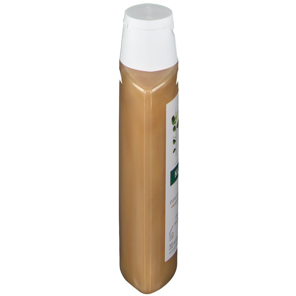 Flacon de shampooing étroit et allongé avec bouchon blanc. Étiquette avec informations produit. Liquide doré visible.