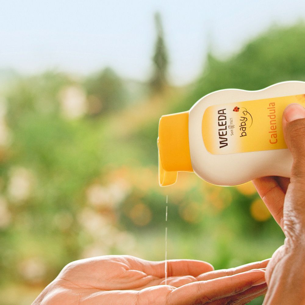 Persoon giet olie uit een Weleda Baby fles in de hand. Gele dop, witte fles, groene omgeving.