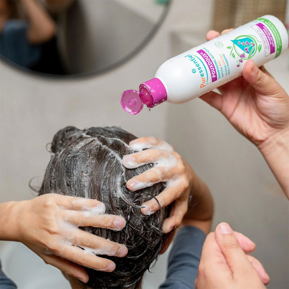 Persoon wast haar met shampoo. Fles met paarse dop. Opschrift: Puressentiel Poudoux®.