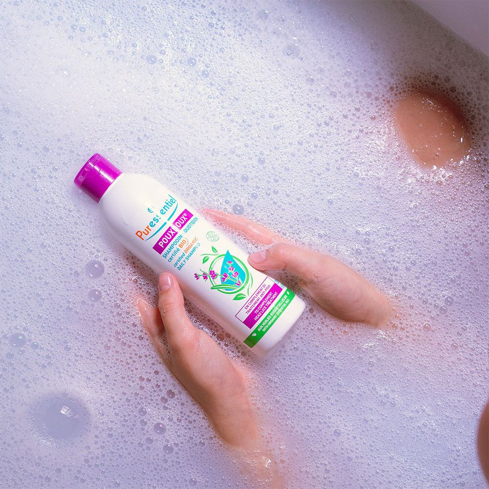 Persoon in bad met shampoo fles. Opschrift: Puressentiel Poudoux®.