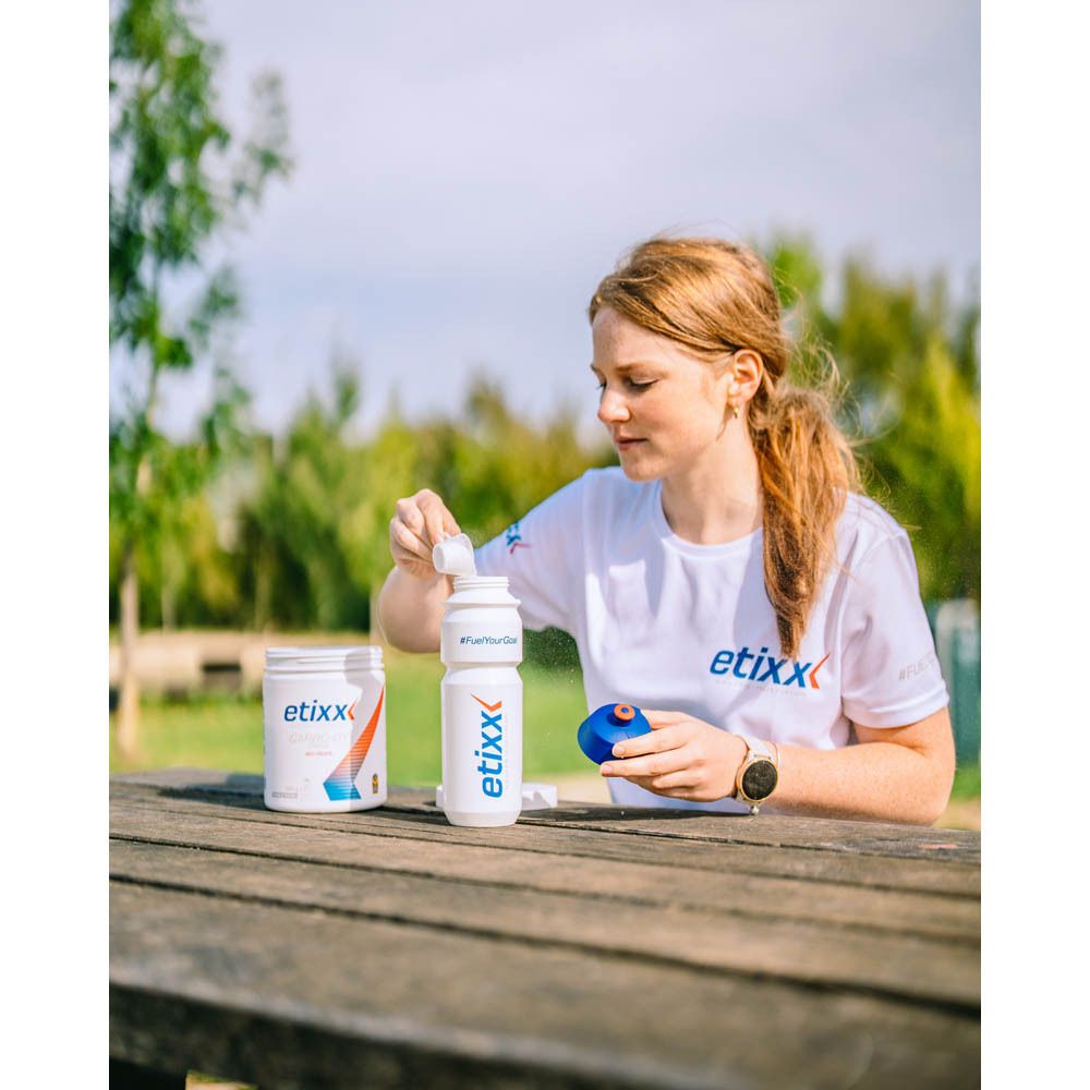 Vrouw aan tafel met etixx-producten. Een drinkfles, een doos en een blauwe dop.