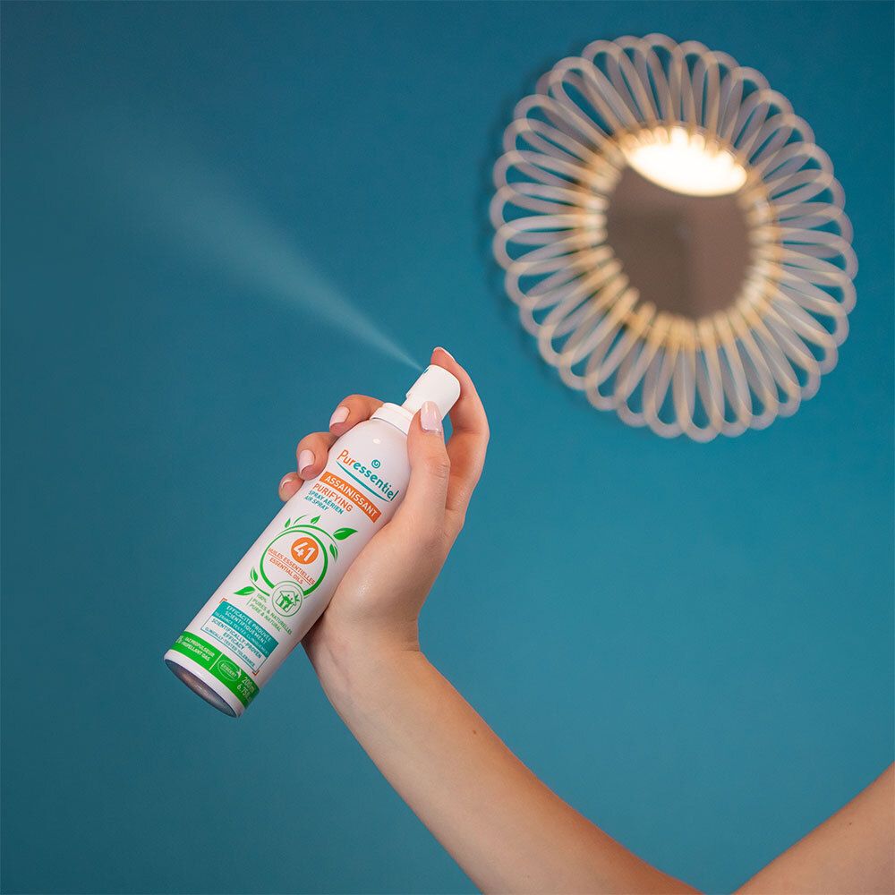Persoon spuit in kamer. Sprayfles met etiket: Puressentiel, Assainissant.