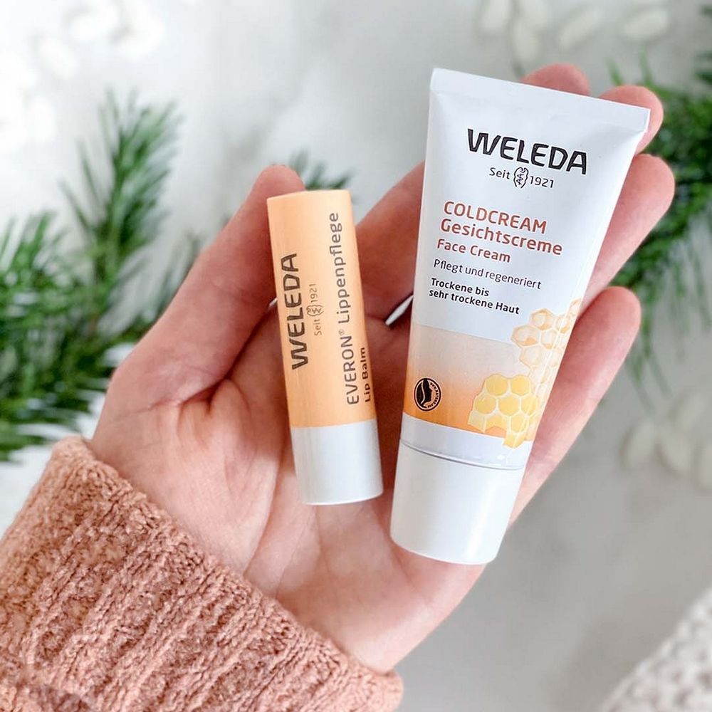 Main tenant deux produits : Coldcream Crème Visage et soin des lèvres. Tous deux de WELEDA. Inscription : EVERON Soin des lèvres.