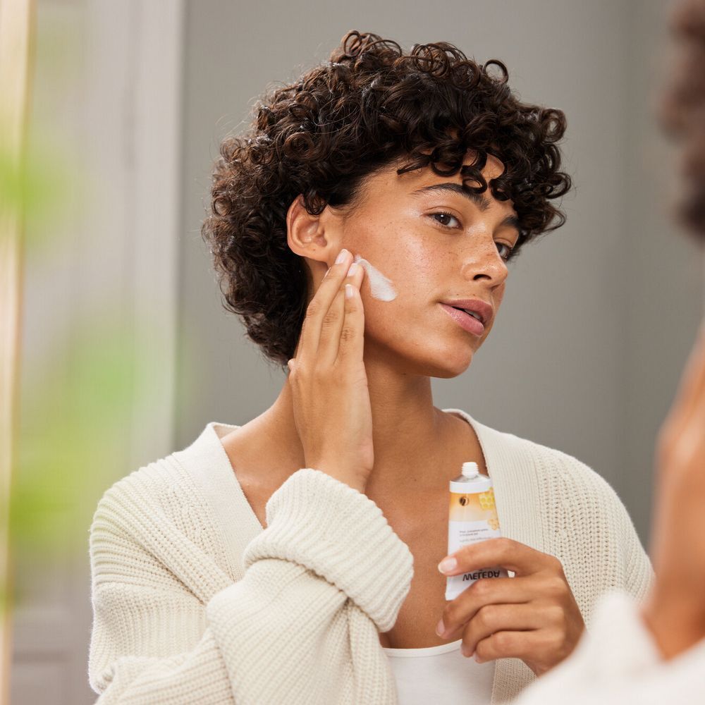 Femme appliquant de la crème sur son visage. Elle tient un tube de Cold Cream de WELEDA.