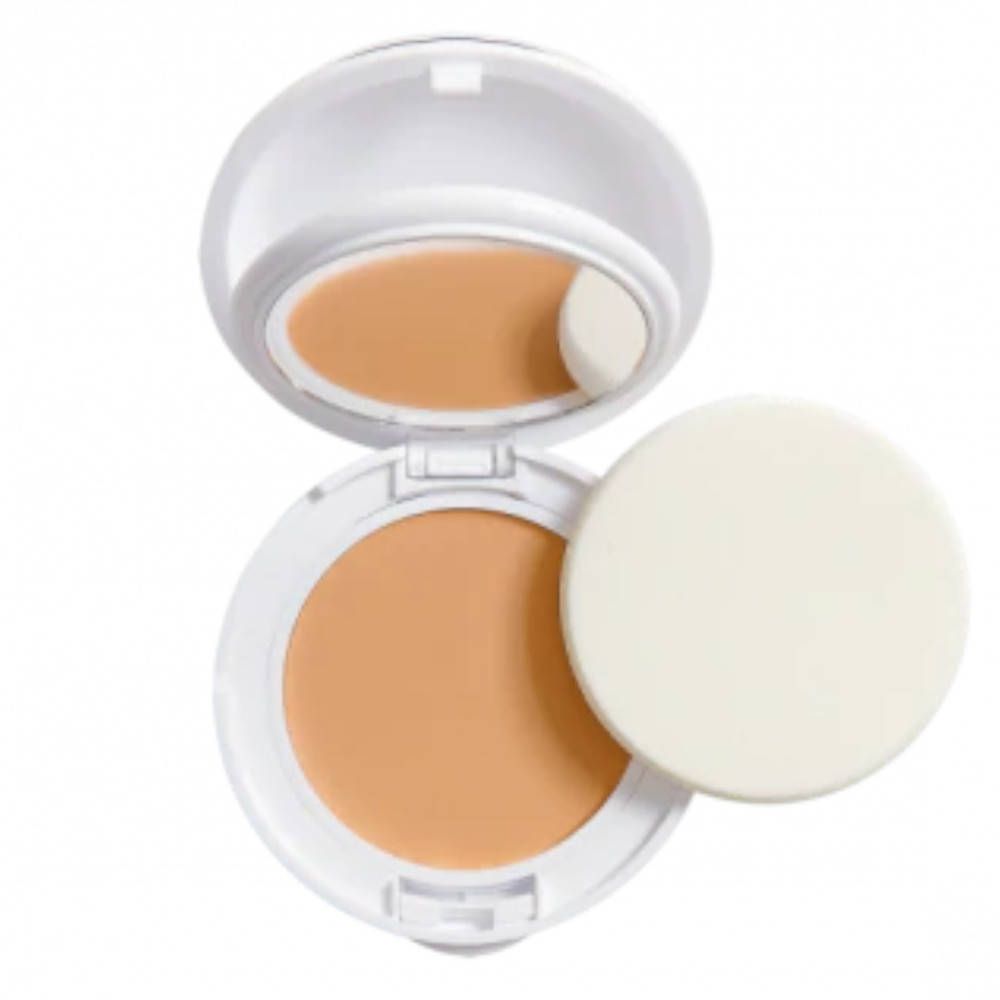 Boîtier de maquillage compact blanc ouvert. Contient du maquillage, un miroir et une éponge. Couleur beige.