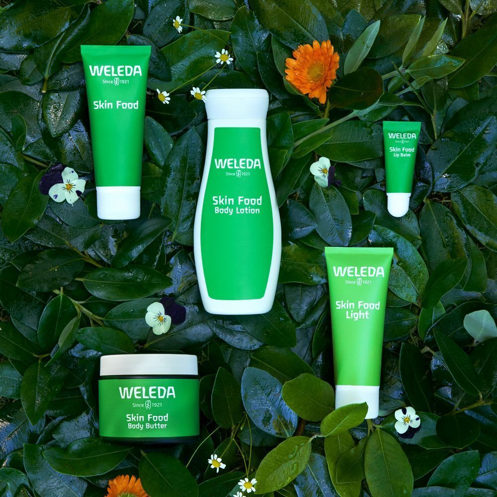 Différents produits Skin Food sur des feuilles. Tubes, pots et flacons. Inscription: WELEDA. Label: 100% cosmétiques naturels certifiés.