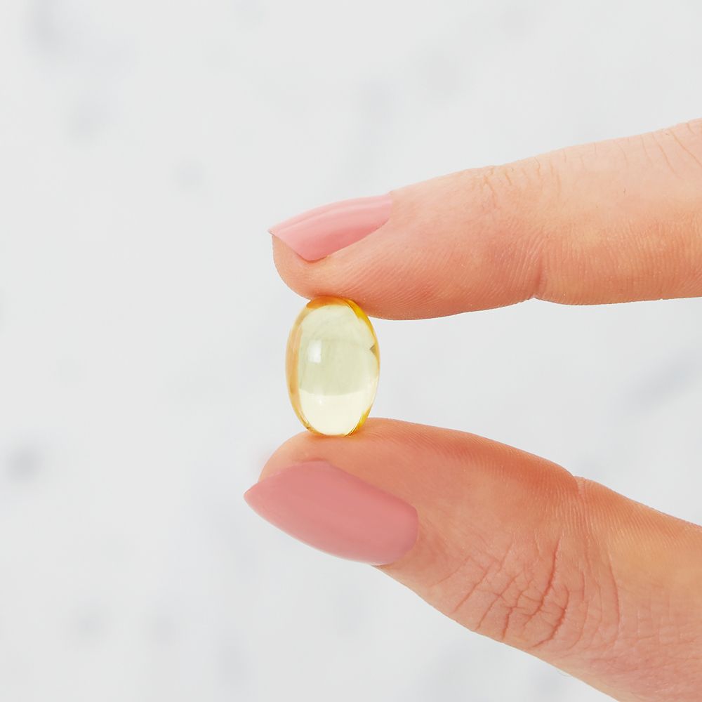 Eine einzelne, gelbe Kapsel zwischen zwei Fingern. Oval, glatt, durchscheinend.