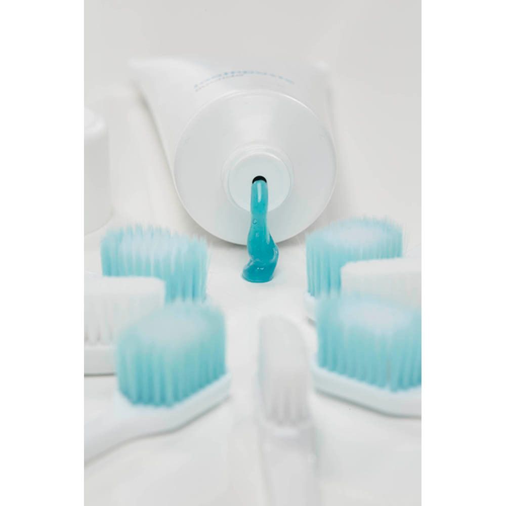 Tube de dentifrice. Du dentifrice bleu est pressé sur plusieurs brosses à dents.