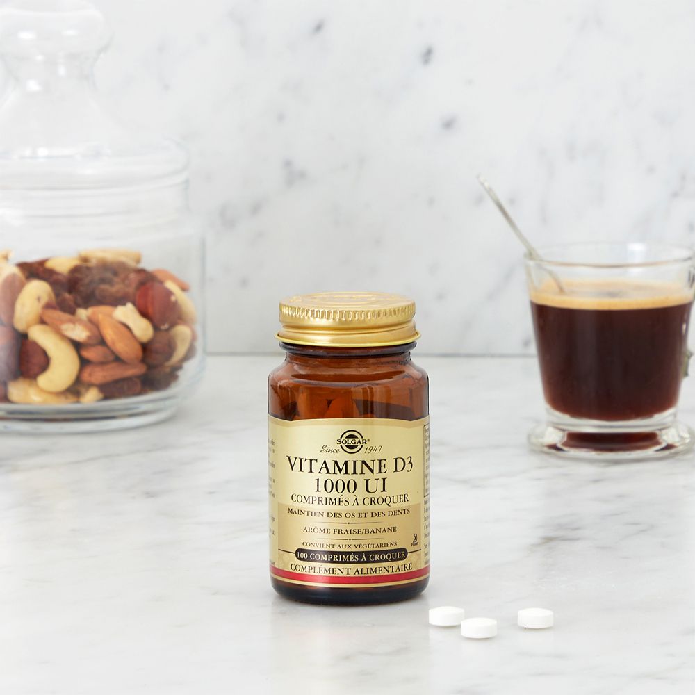 Kleine bruine fles SOLGAR® VITAMIN D3, 1000 IE, naast glas met noten en koffie. Enkele tabletten ernaast.