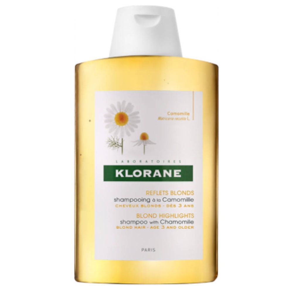 Flacon de shampooing Klorane à la camomille. Contenu jaune, bouchon blanc. Étiquette avec fleurs de camomille et texte.