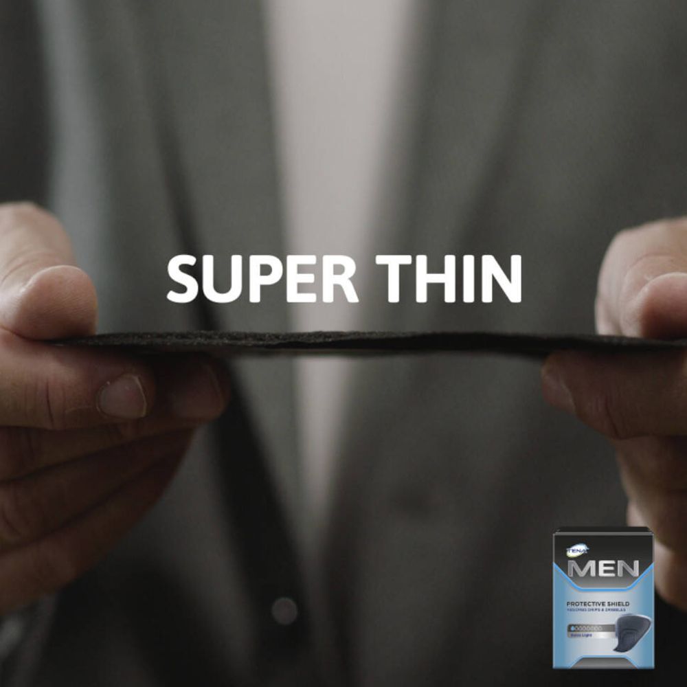 Hände halten ein schwarzes TENA Men Protective Shield. Text: SUPER THIN. Kleines Produktbild in der Ecke.