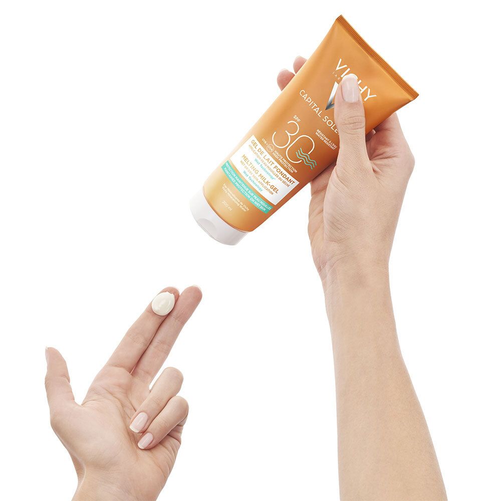 Main avec produit sur le doigt. Tube en arrière-plan. Inscriptions: VICHY, CAPITAL SOLEIL, SPF 30.
