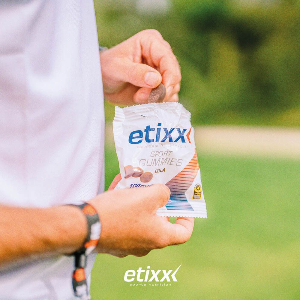 Personne tenant un sachet de Sport Gummis etixx®. Goût cola. 100mg sodium. Sport Banned Substances Tested.