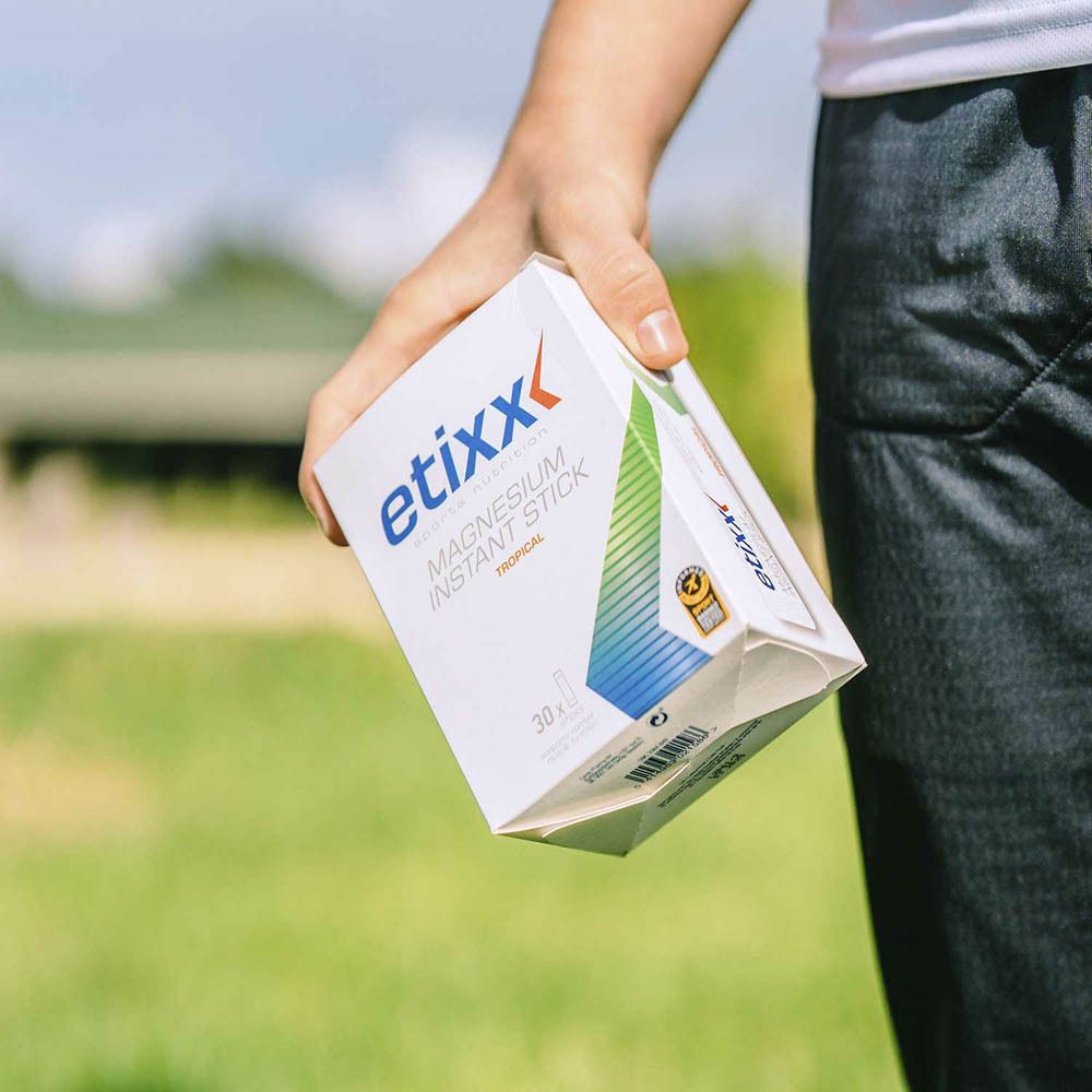 Boîte Etixx Magnesium Instant Stick tenue en main. Boîte blanche avec logo et informations. Fond vert.